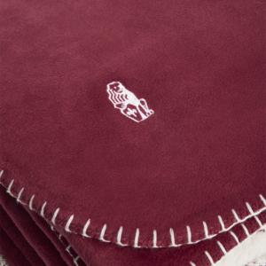 Gefaltete Sofadecke in Bordeauxrot mit weicher, weißer Sherpa-Fleece-Innenseite und dekorativer Ziernaht – ideal für gemütliche Stunden auf dem Sofa