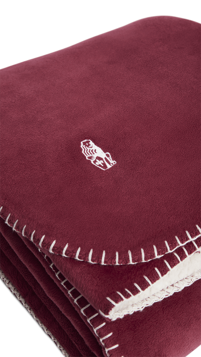 Gefaltete Sofadecke in Bordeauxrot mit weicher, weißer Sherpa-Fleece-Innenseite und dekorativer Ziernaht – ideal für gemütliche Stunden auf dem Sofa
