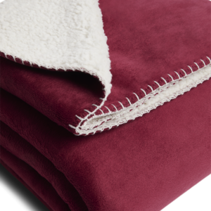 Gefaltete Sofadecke in Bordeauxrot mit weicher, weißer Sherpa-Fleece-Innenseite und dekorativer Ziernaht – ideal für gemütliche Stunden auf dem Sofa