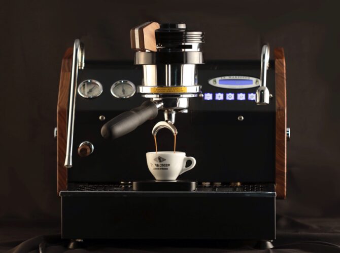 Eine La Marzocco Espressomaschine in edlem Schwarz mit Holzdetails zieht im stilvollen Setup alle Blicke auf sich. Die professionelle Siebträgermaschine brüht gerade einen doppelten Espresso direkt in die klassische La Marzocco Tasse. Ausgestattet mit Dualboiler, präziser Brühgruppe, digitalem Display und Barista-Steuerung – ideal für Kaffee-Enthusiasten, professionelle Baristas und anspruchsvolle Café-Umgebungen. Maximale Kontrolle für perfekte Kaffeezubereitung.