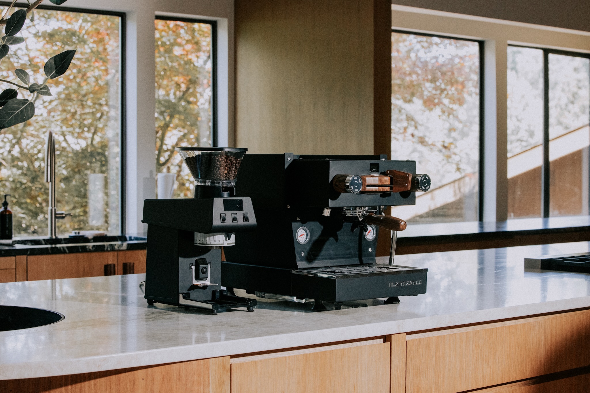 Schwarze La Marzocco Siebträgermaschine mit Holzgriffen und Espressomühle auf Kücheninsel, hochwertige Espressomaschine für Gastronomie oder anspruchsvollen Kaffeegenuss zuhause im modernen Umfeld
