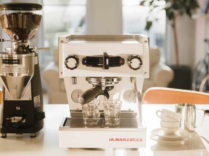 Weiße La Marzocco Siebträgermaschine mit Espressomühle auf heller Küchenzeile, zwei Espressogläser im Bezug, professionelle Espressomaschine für Gastronomie und anspruchsvollen Kaffeegenuss zu Hause